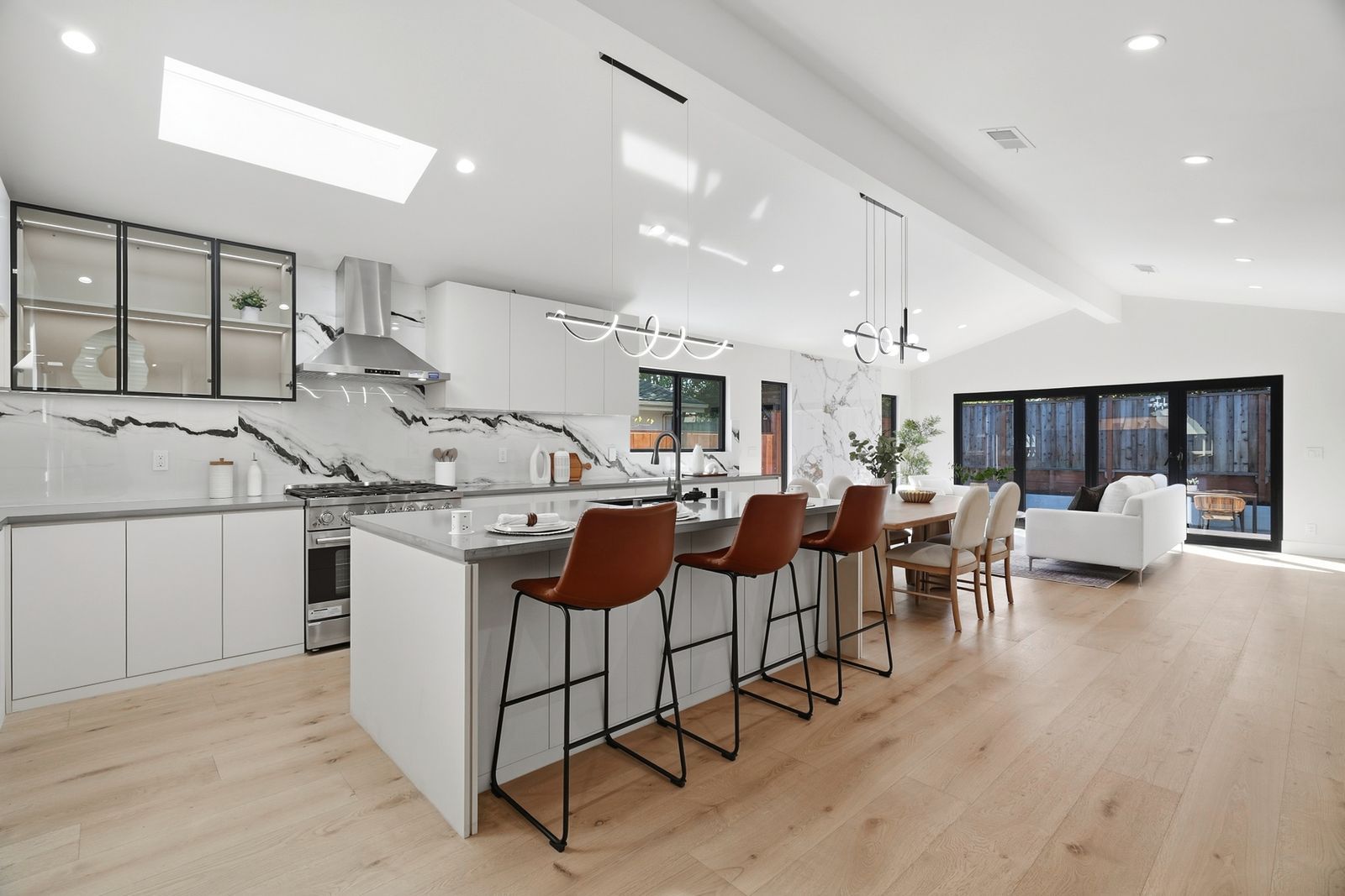 Open kitchen with a long island, leather bar stools and a marble slab backsplash